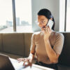 Lächelnde Frau mit dem Smartphone in der Hand. Sie nutzt onOffice enterprise am Laptop.