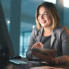 Woman in front of desktop computer with tablet in hand