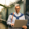 Man wearing glasses using a laptop in front of a modern glass building