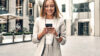 Frau in der Stadt am Handy die nach Immobilien Trends sucht