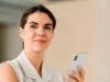 Frau die ihr Handy in der Hand hat und in die Kamera guckt