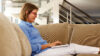 Eine Frau liegt mit ihrem Laptop auf den Beinen auf der Couch.