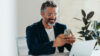 Lachender Mann vor Smartphone und Laptop