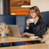 A young woman is sitting at a café working on her laptop