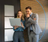 Eine Frau und ein Mann in einem modernen Büro schauen gemeinsam auf einen Laptop