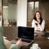 Zwei Frauen sitzen an einem Meetingtisch mit Laptop und Tablet