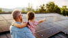 Mann mit Kind auf dem Arm das auf Dach mit PV-Anlage zeigt